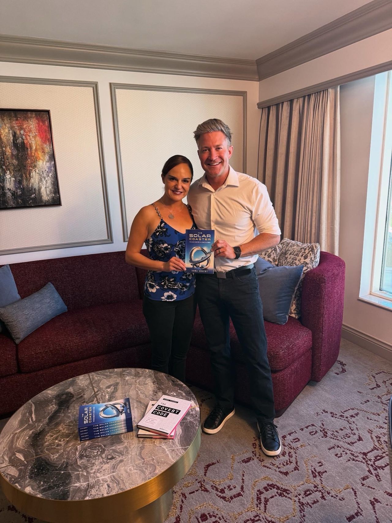 Anna Covert and Ryan Park holding The Solar Coaster book, with The Covert Code displayed on the table